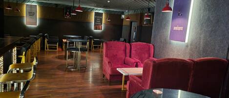 Interior de restaurante con suelo de madera, asientos tapizados en rojo e iluminación colgante.
