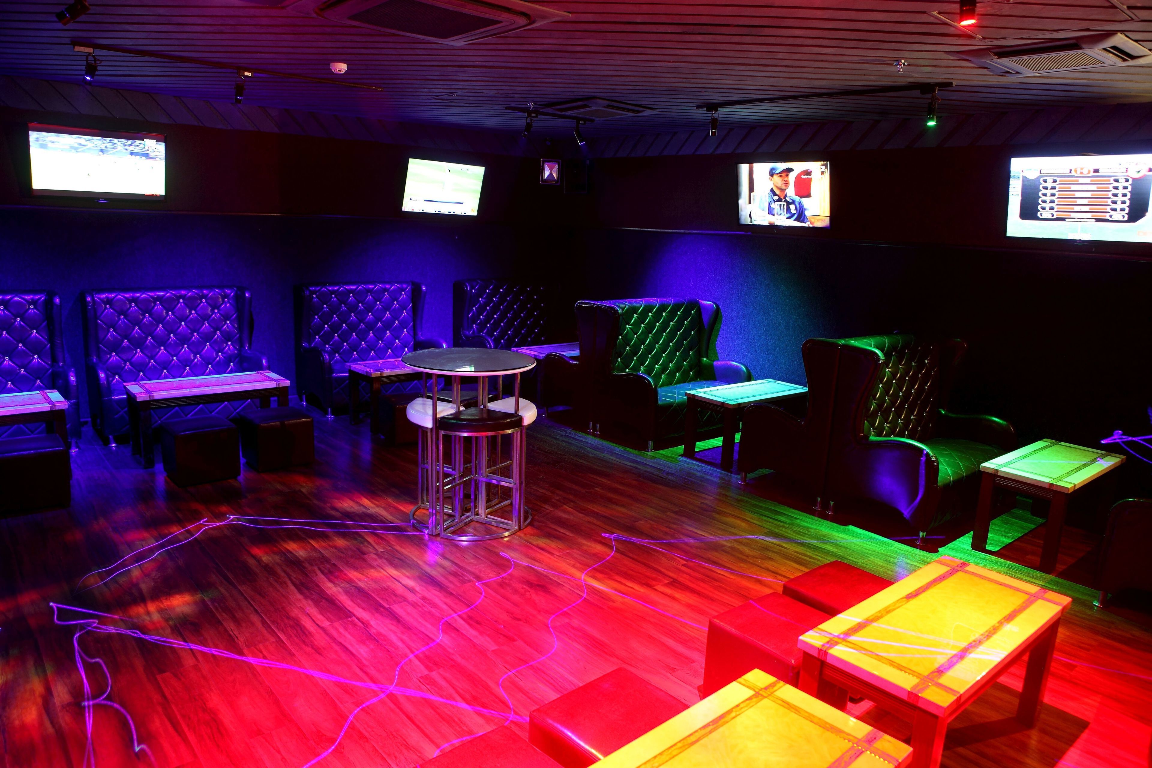 A room with multiple seating areas, including cushioned booths and tables, with a wooden floor and overhead lighting.