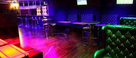 A bar area with stools, tables, and a television screen.