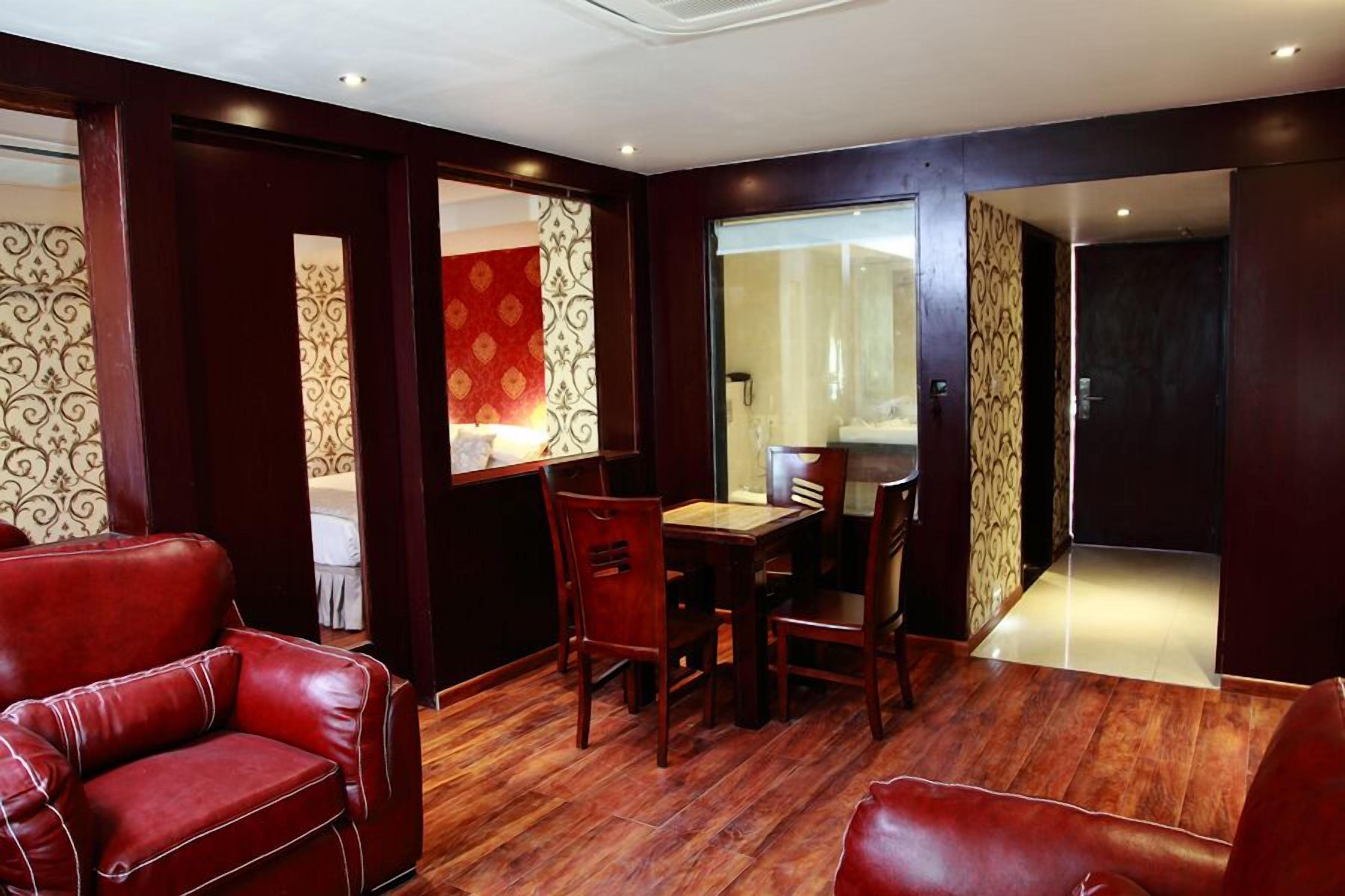 A room with a wooden floor, a dining table with chairs, and a red leather sofa.