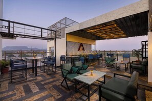 Un espacio al aire libre con mesas, sillas, un bar y vistas de la ciudad.