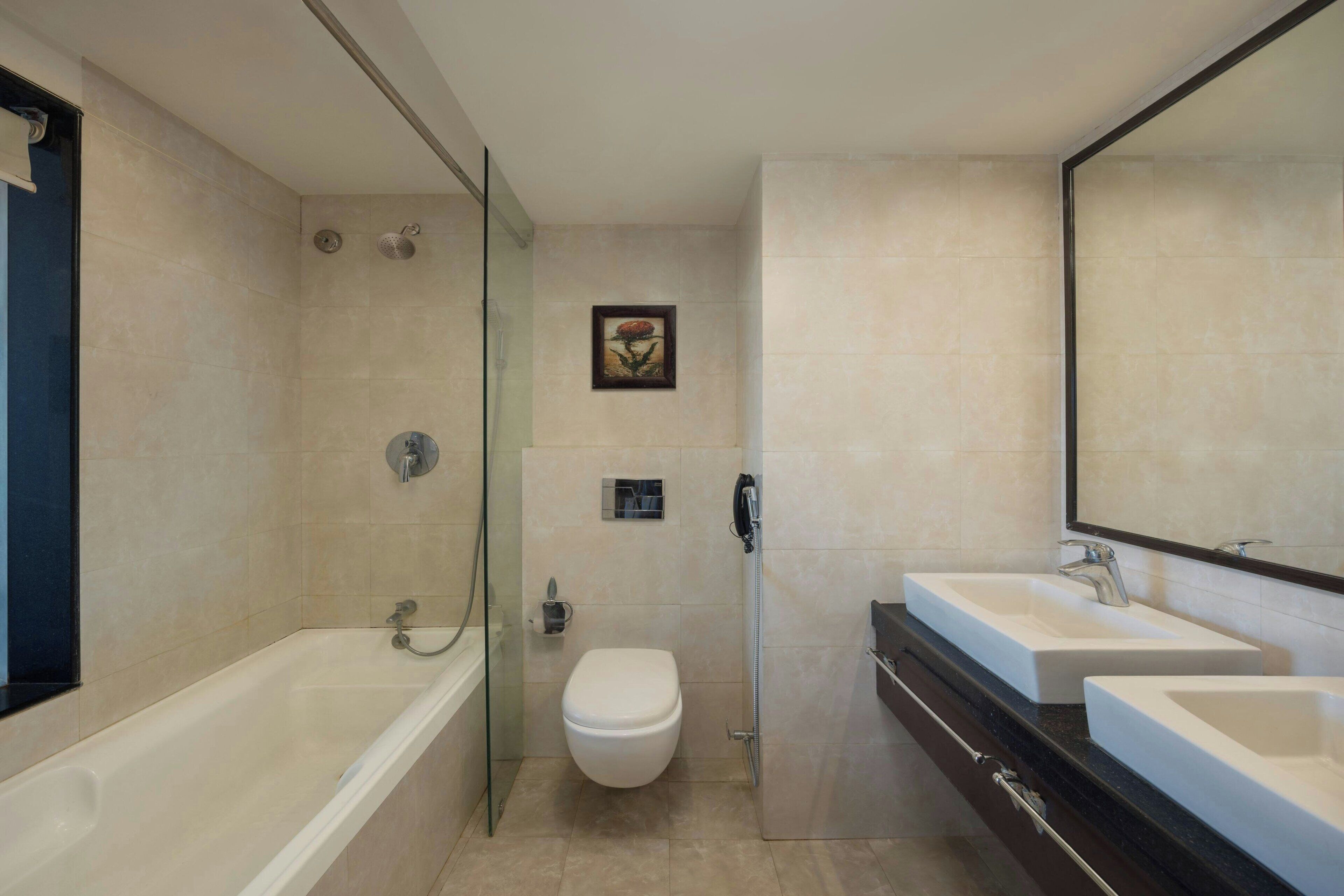 A modern bathroom with a glass-enclosed shower, a toilet, and two sinks with a large mirror above.