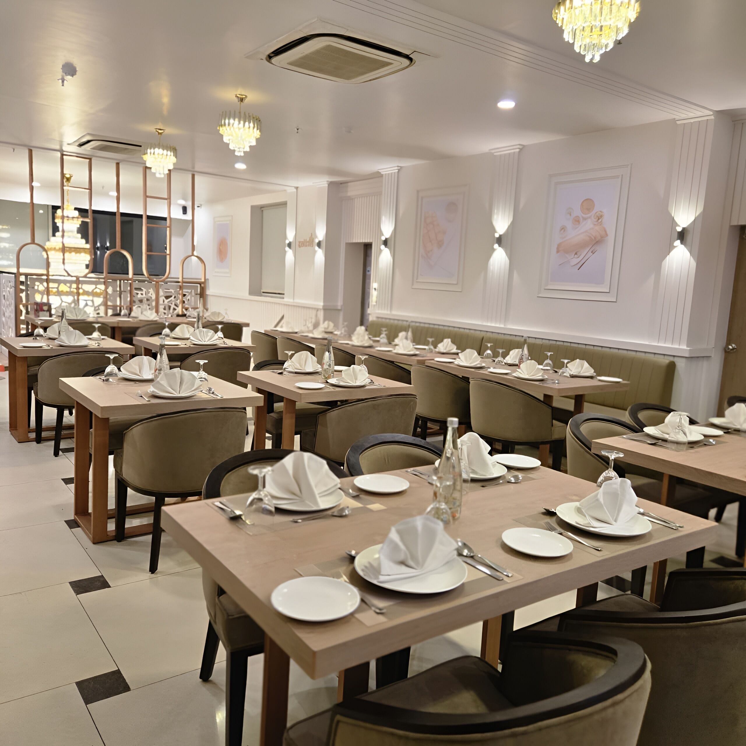 A restaurant with multiple tables set for dining, featuring a modern interior with chandeliers and wall-mounted lighting.