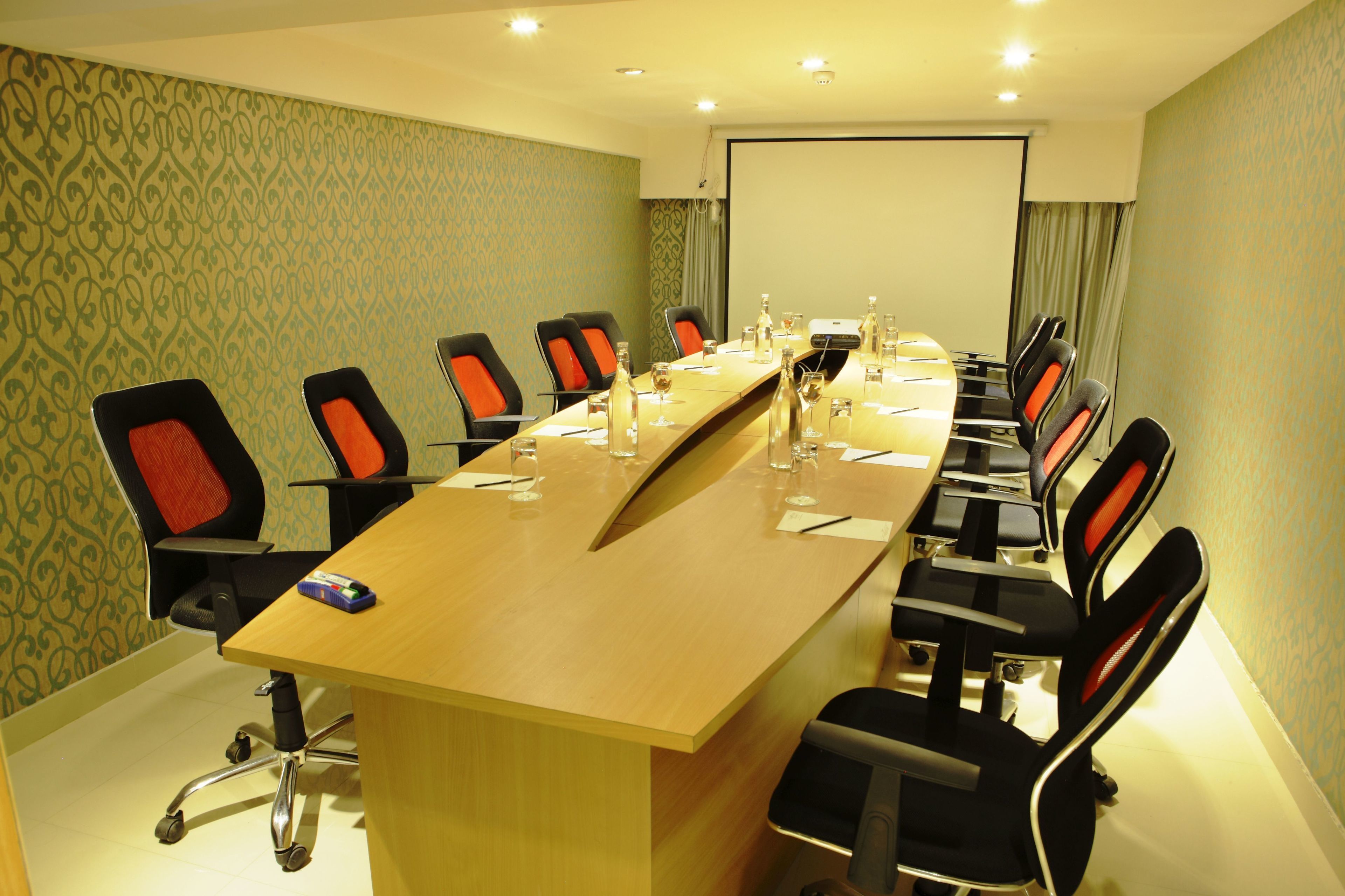 Sala de conferências com uma mesa comprida, cadeiras e tela de projeção.