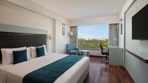 A modern hotel room with a large bed, a desk, a chair, and a TV.