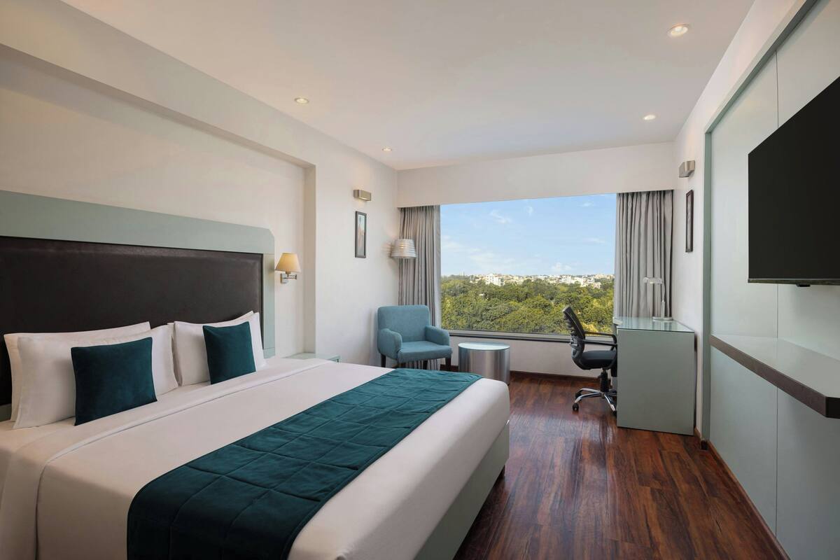Ein modernes Hotelzimmer mit einem großen Bett, einem Schreibtisch, einem Sessel und einem Fernseher.