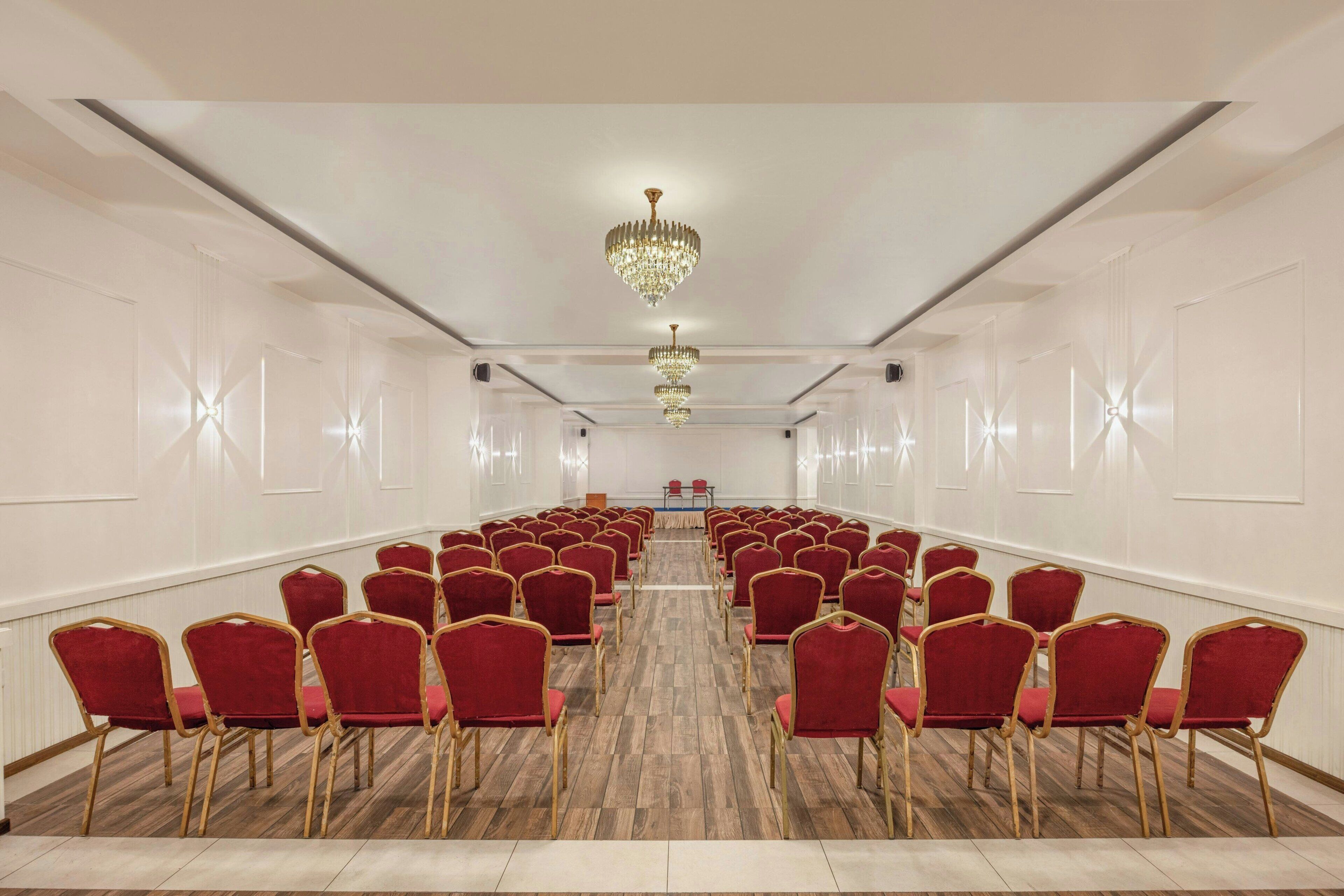 A conference room with rows of red chairs and a long table at the front.