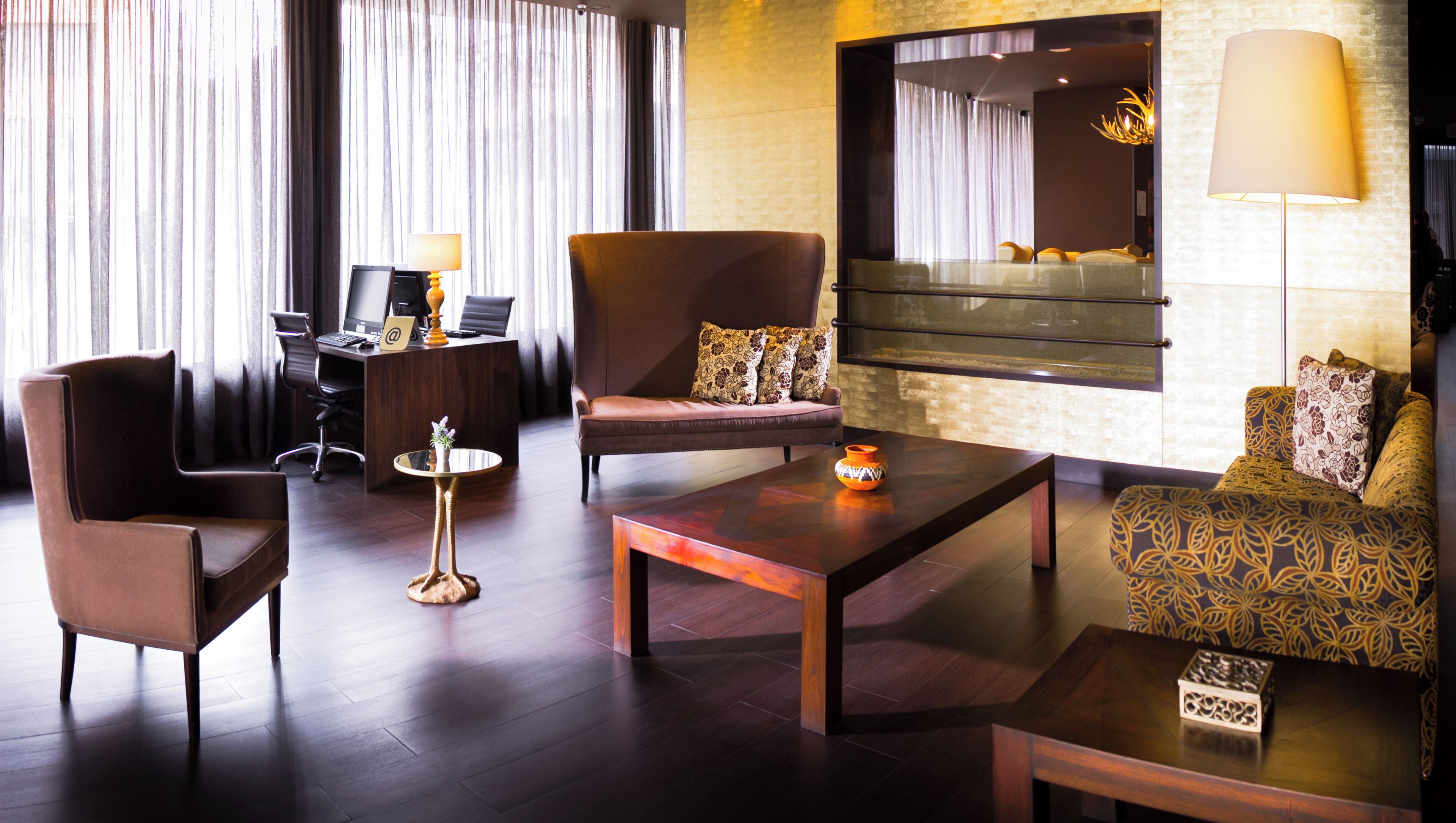 A modern hotel room with a seating area, a desk, and a large window with curtains.