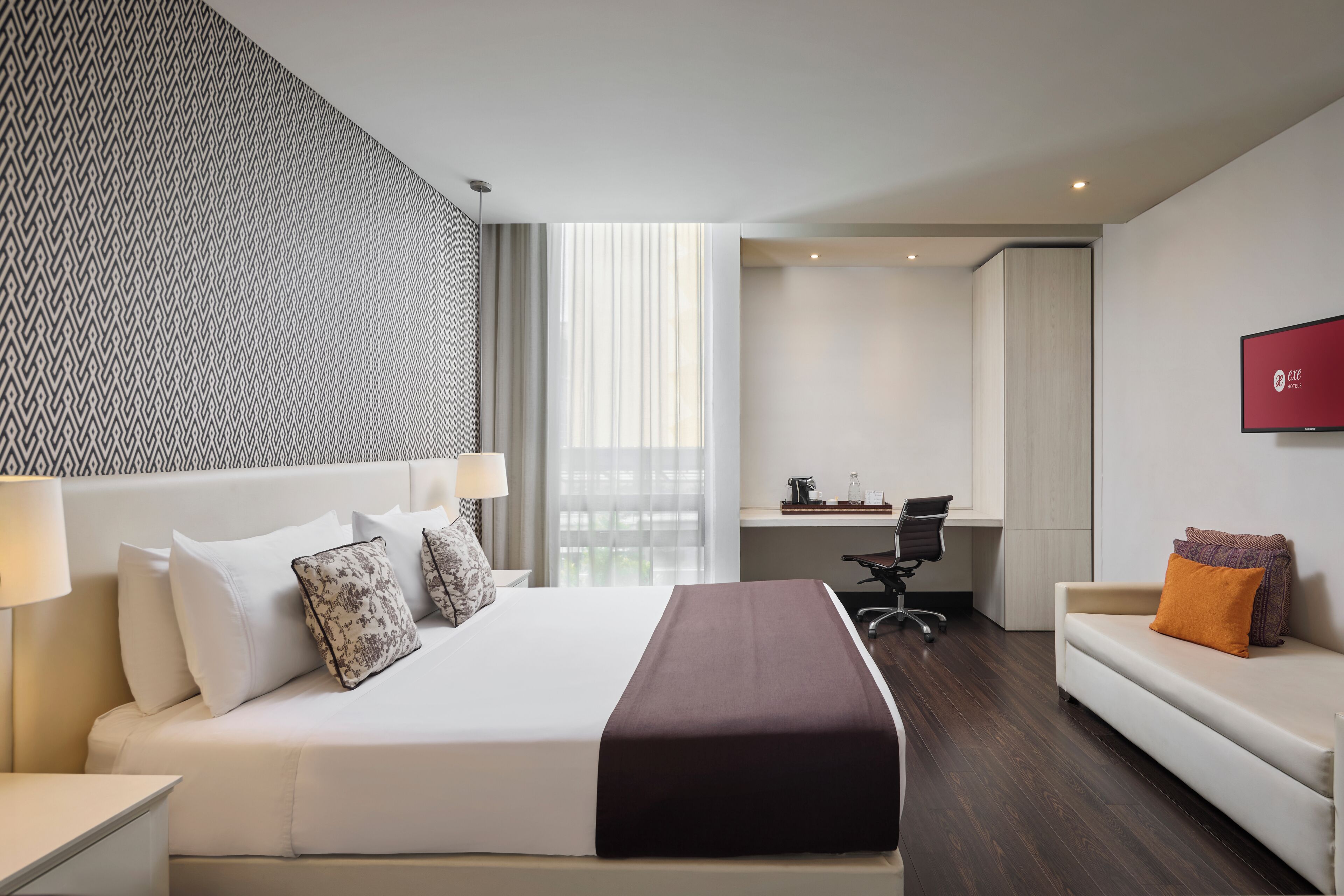 A hotel room with a large bed, a desk, a chair, and a sofa.
