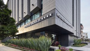 A modern hotel exterior with a name sign, large windows, and a landscaped garden area. - Hotel Exe Bacata 95 (Bogotá)
