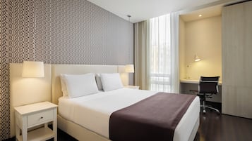 A hotel room with a large bed, a desk, and a chair.