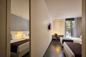 Una camera d'albergo moderna con un letto grande, una scrivania con sedia, una TV fissata al muro e una finestra con tende.
