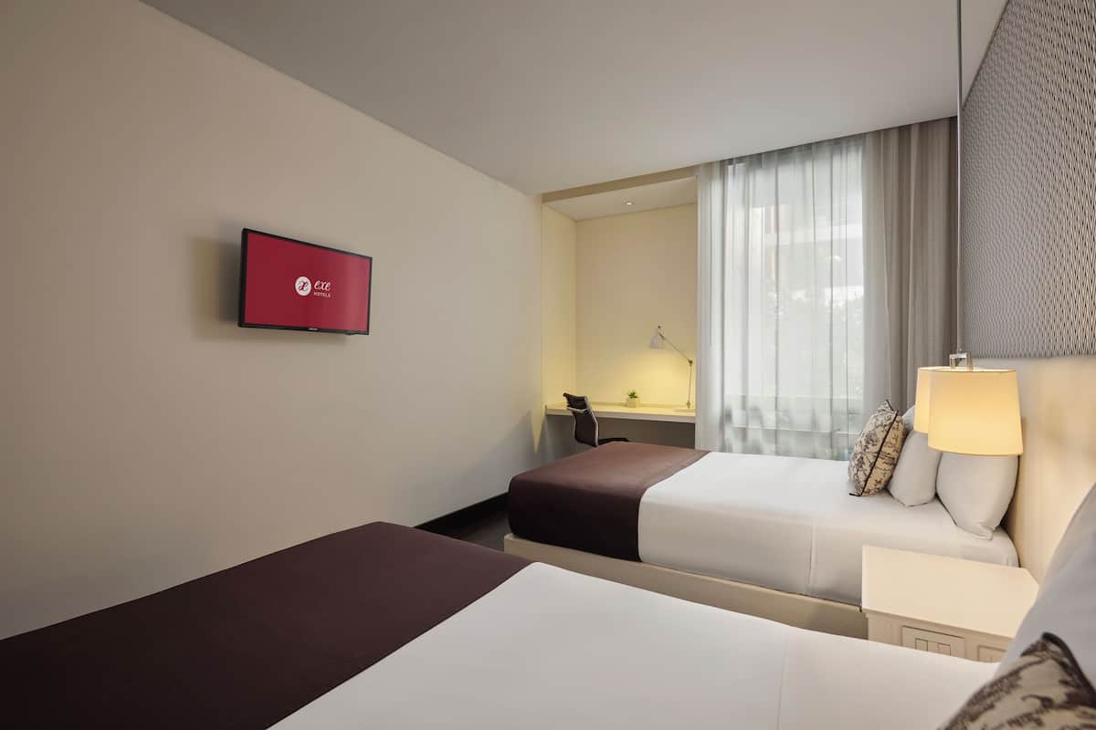 Habitación de hotel con dos camas, un escritorio con lámpara, televisor en la pared y ventana con cortinas.
