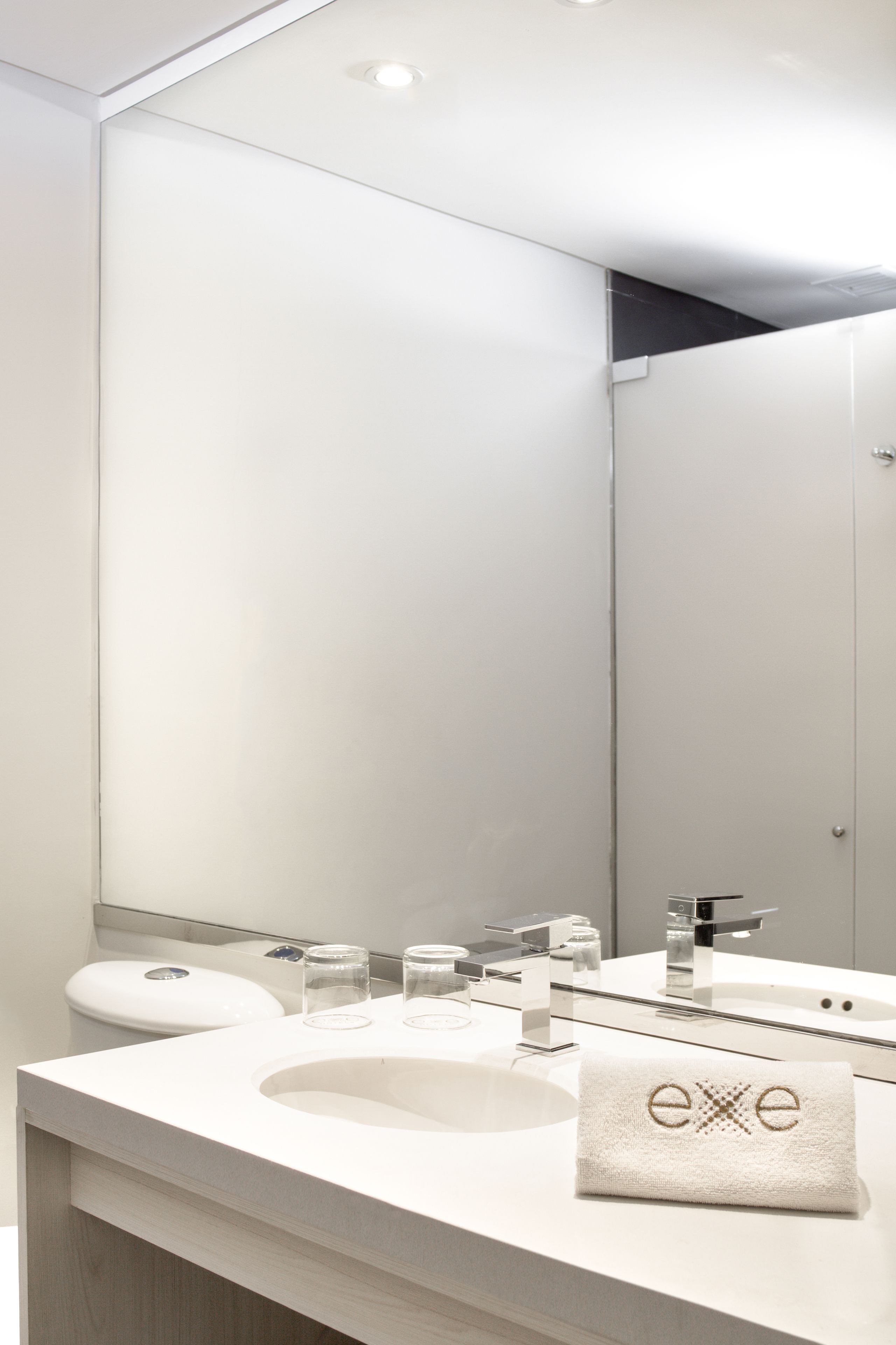 Une salle de bain moderne avec un grand miroir, un lavabo et une serviette ornée du motif « exe ».