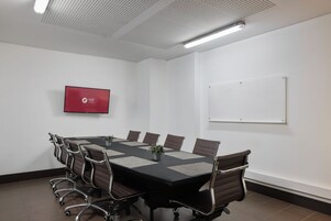 Ein Konferenzraum mit einem langen Tisch, sechs Stühlen, einem Fernsehbildschirm und einer Whiteboard-Tafel.