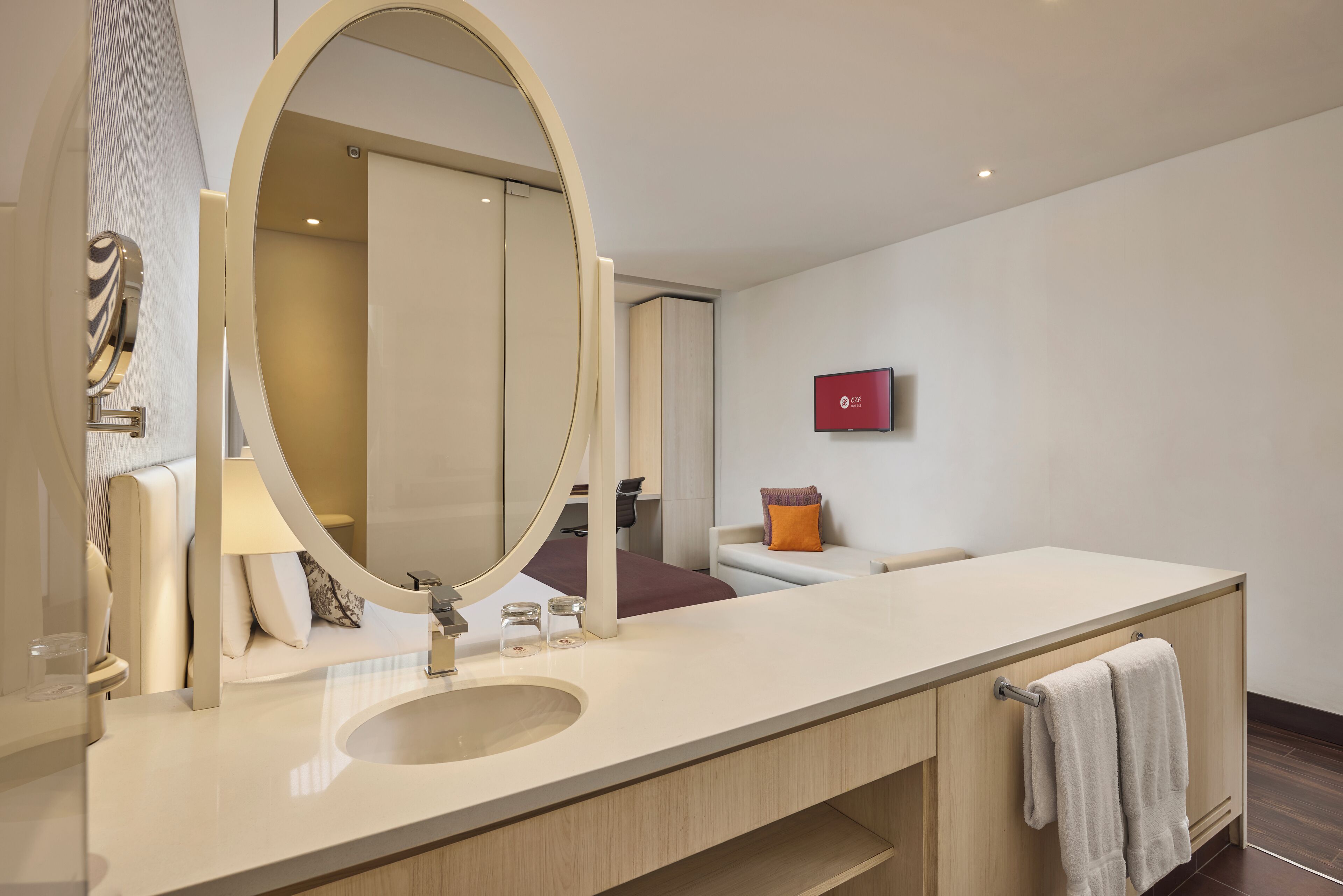 A modern bathroom with a large oval mirror, a sink, and a towel rack.