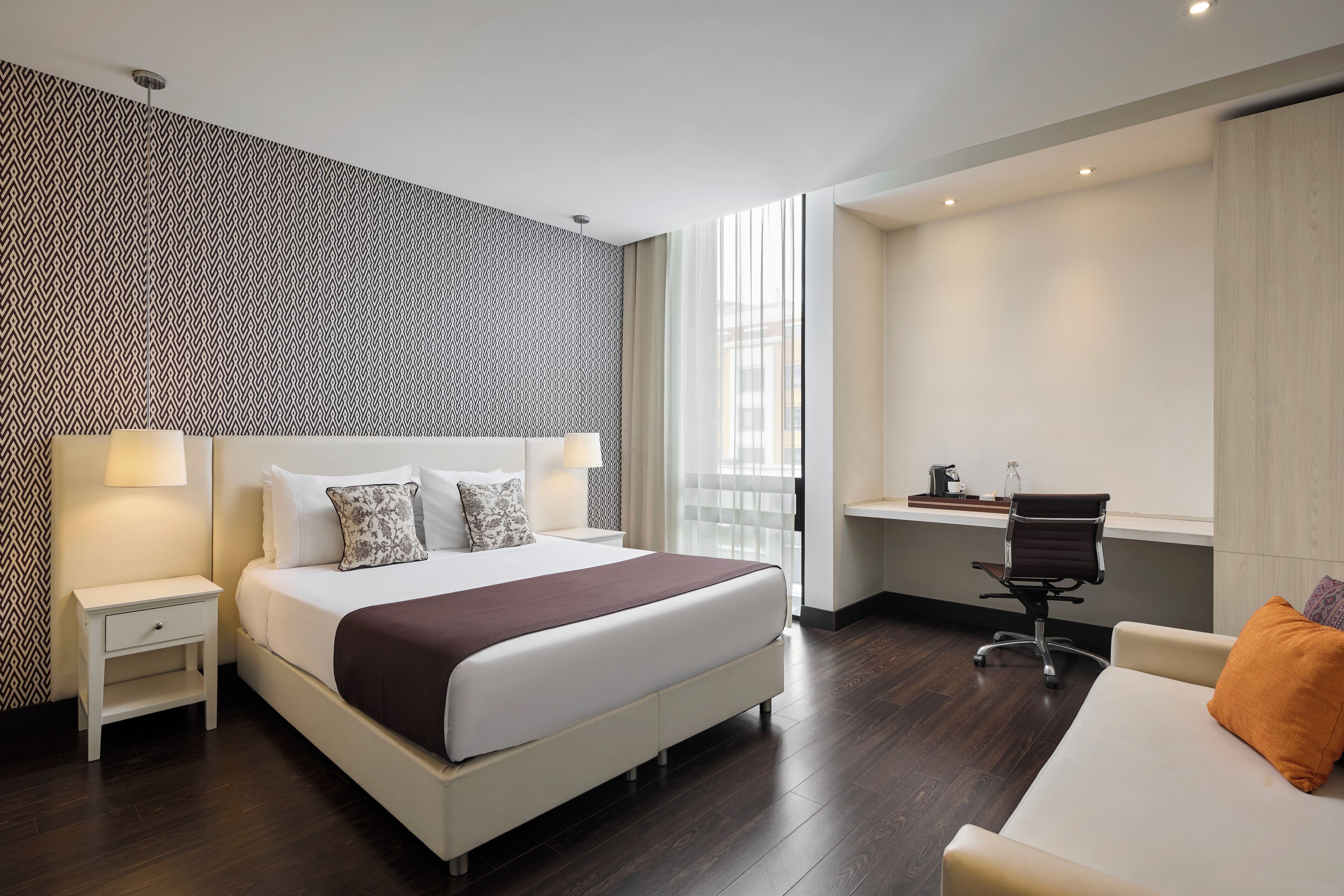 A modern hotel room with a large bed, a desk, and a chair.