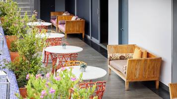 Una terraza en la azotea con mesas redondas, sillas de mimbre, plantas en macetas y un sofá.