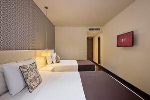Habitación de hotel con dos camas, un televisor montado en la pared y un papel tapiz estampado.
