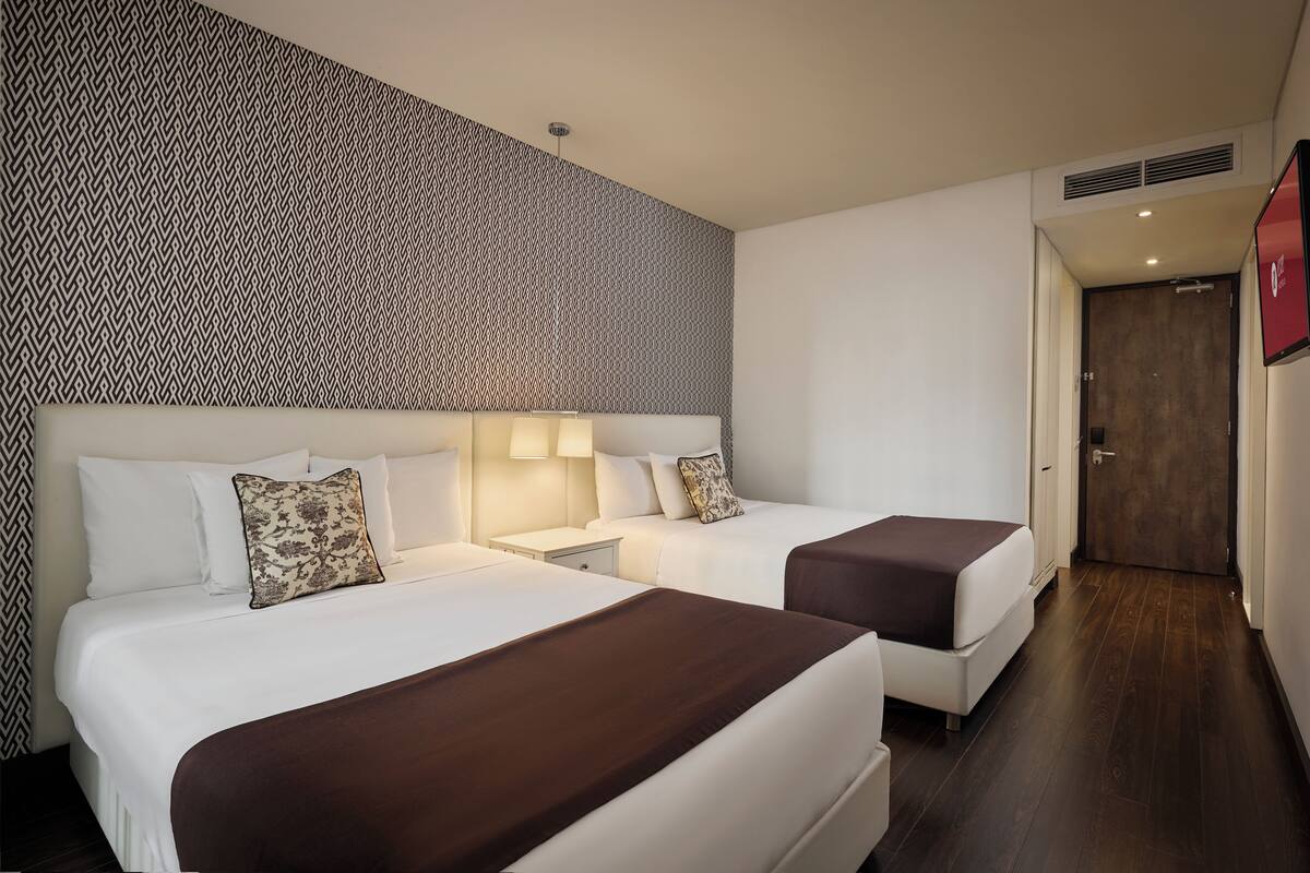 Habitación de hotel con dos camas, un papel tapiz estampado, suelo de madera y una puerta.