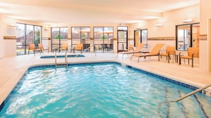 An indoor swimming pool with clear water, surrounded by lounge chairs and a view of the outdoors.