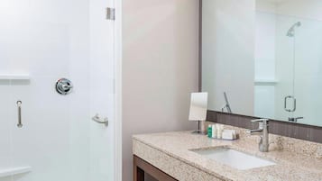 A modern bathroom with a glass shower enclosure, a sink with a marble countertop, and a mirror above the sink.