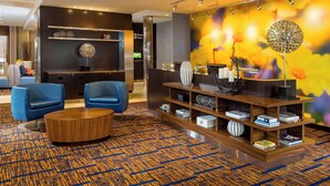A modern lobby with a patterned carpet, blue chairs, a wooden coffee table, and a decorative wall with a spherical ornament.