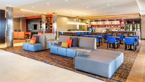 A modern hotel lobby with a seating area, a bar, and a restaurant.