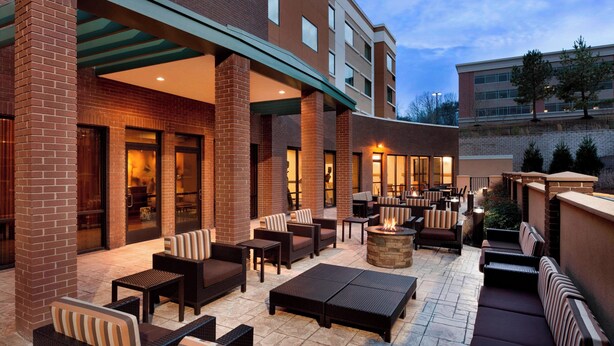 An outdoor patio area with seating arrangements, a fire pit, and a covered walkway.