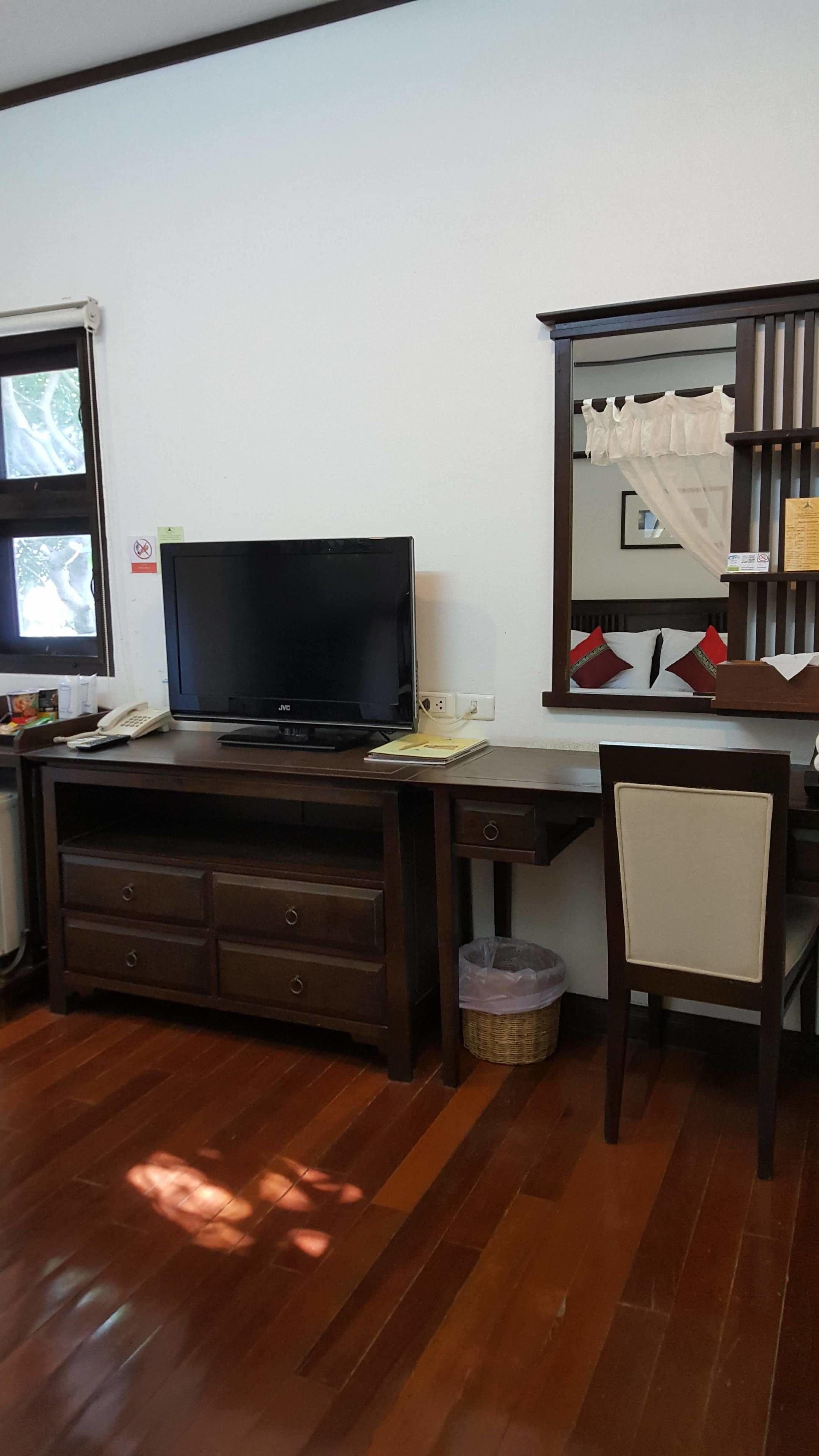 Una habitación con un escritorio de madera, televisión, una silla, ventana y espejo.