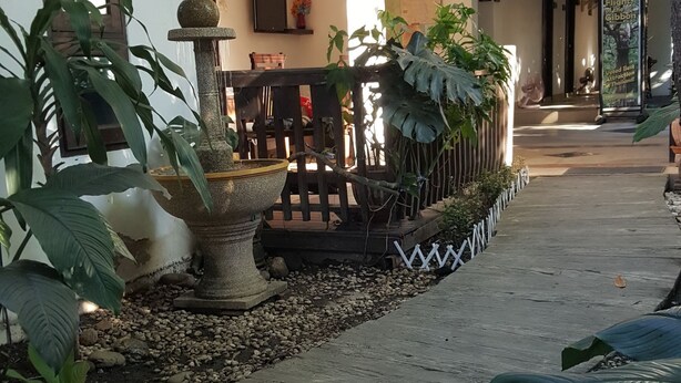 A covered outdoor area with a wooden deck, potted plants, and a stone fountain. - Ping Phu Place (Chiang Mai)