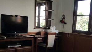A room with a television, wooden desk, chair, and a window with a view of greenery. - Ping Phu Place (Chiang Mai)