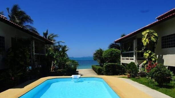 A swimming pool with a view of the ocean, surrounded by greenery and two buildings with red roofs. - New Sunrise Village Bang Po Beach (Koh Samui)