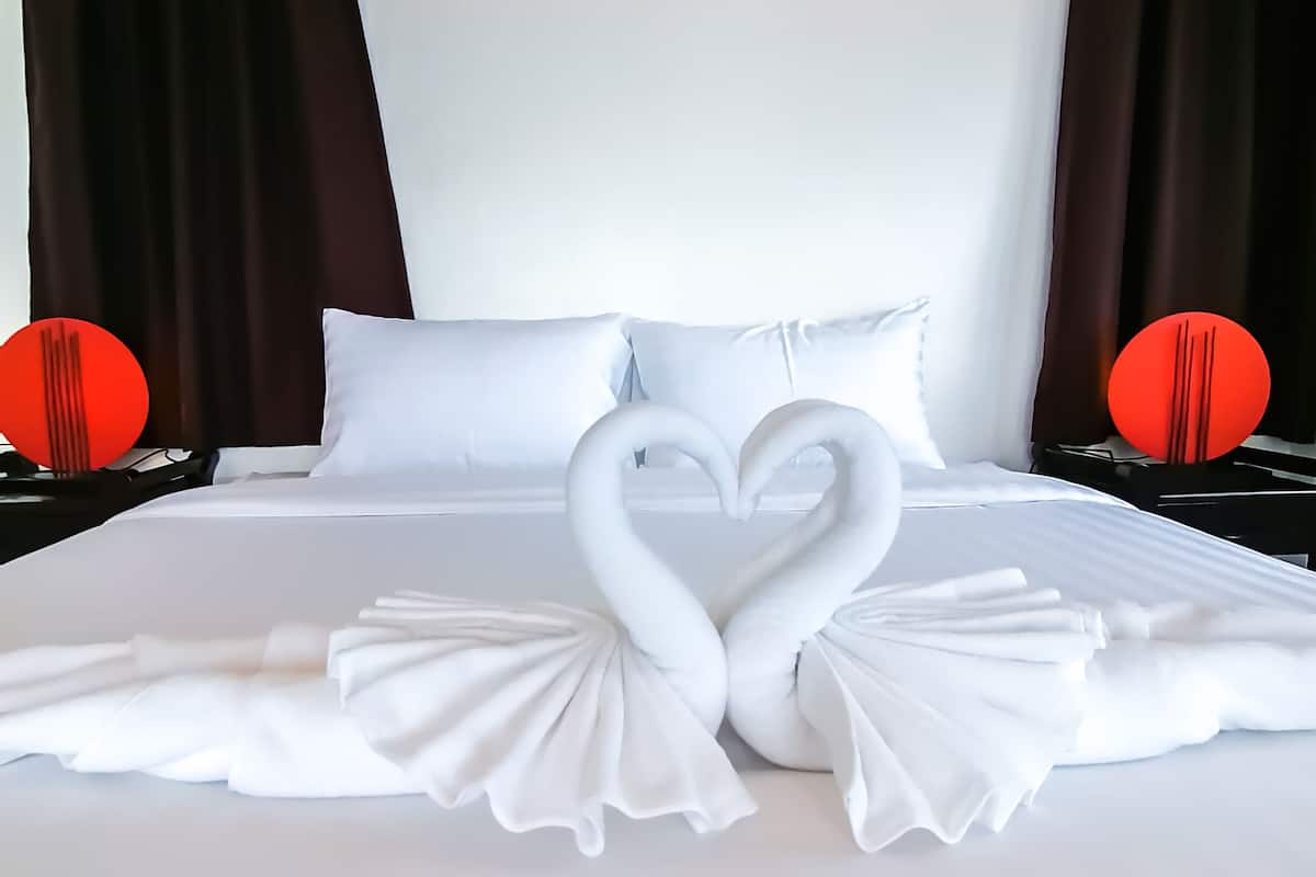 A neatly made bed with white linens and two swan-shaped towels arranged on the bed.
