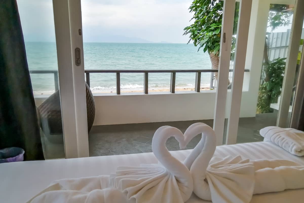 A room with a view of the sea, a heart-shaped towel arrangement, and a plant.