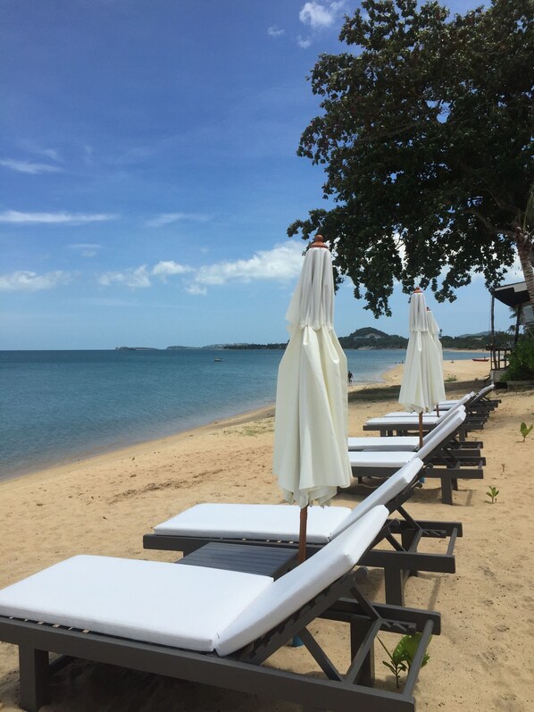 A beach with lounge chairs and umbrellas, a clear sky, and calm sea. - The Cosy Beach Resort (Koh Samui)