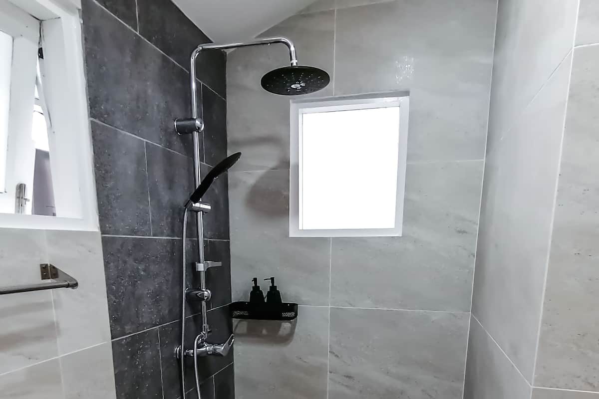 A modern bathroom with dark tiles, a shower, and a small window.