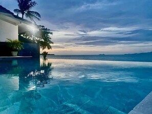 An infinity pool with clear blue water, a palm tree, and a view of the ocean at sunset. - The Cosy Beach Resort (Koh Samui)