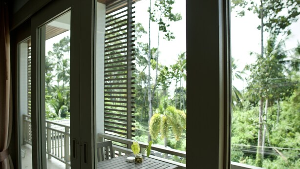 A balcony with a wooden table and a small vase of flowers, overlooking a lush green landscape with trees and a railing. - Ampha Place Hotel (Koh Samui)