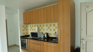 A compact kitchen with wooden cabinets, a microwave, a kettle, and a sink. - Ampha Place Hotel (Koh Samui)