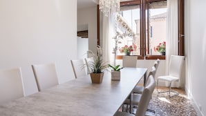 A dining area with a long table, white chairs, and potted plants.