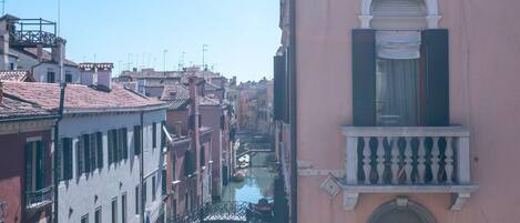 Un canal avec des bateaux, un bâtiment rose doté d’un balcon, et des fleurs rouges au premier plan.