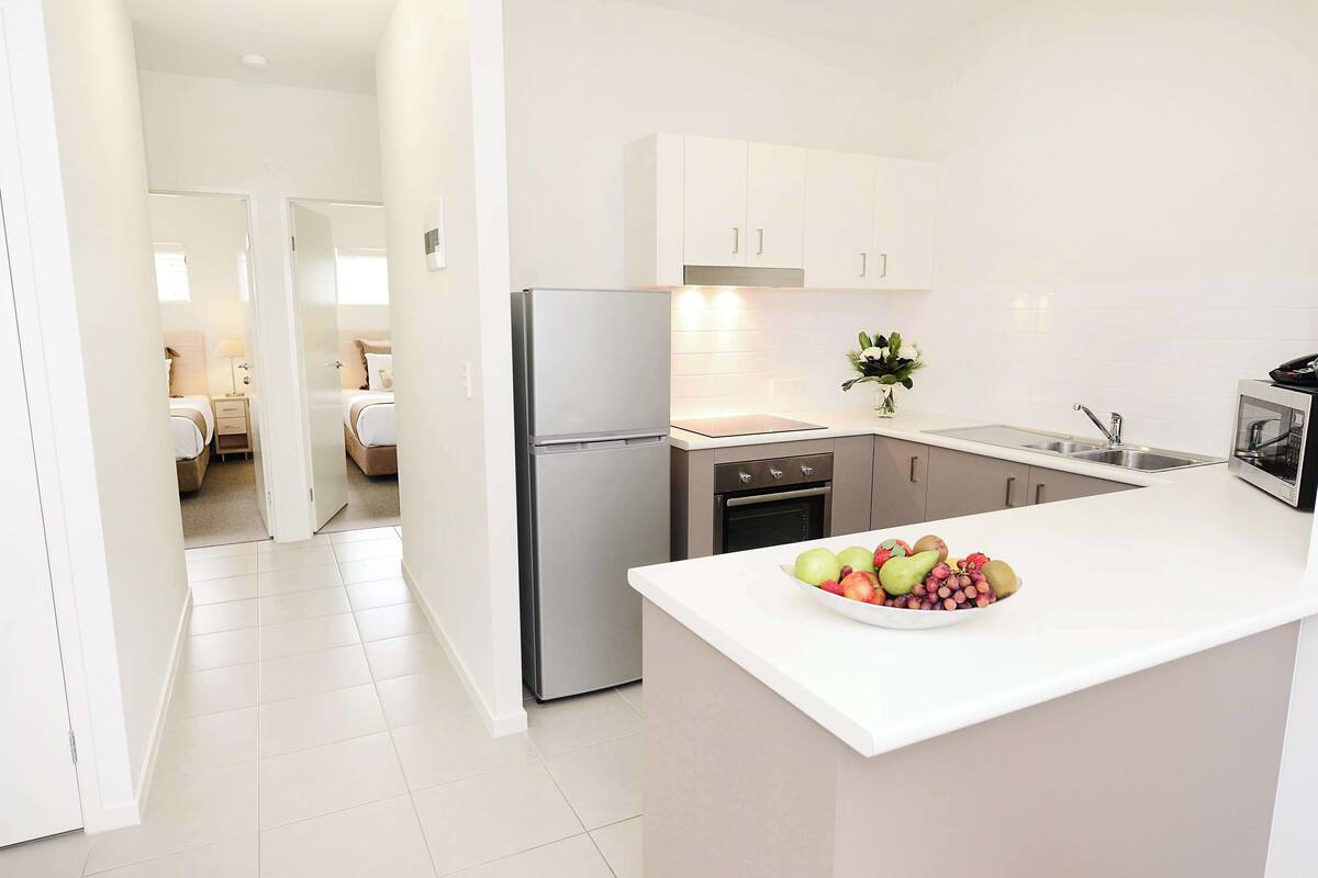 A modern kitchen with white cabinets, a stainless steel refrigerator, and a fruit bowl on the counter.