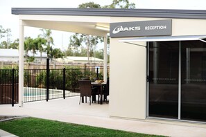 A reception area with a sign reading "OAKS RECEPTION," a covered patio with a table and chairs, and a pool in the background.