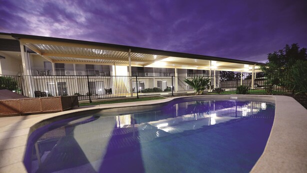 A swimming pool with a covered patio area and a building in the background. - Oaks Middlemount Suites (Middlemount)