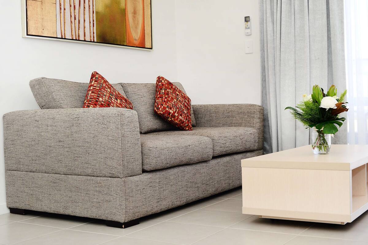 A modern living room with a grey sofa, two patterned throw pillows, a white coffee table, and a vase with flowers.