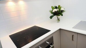 A modern kitchen with a black induction cooktop, stainless steel cabinets, and a white countertop. - Oaks Middlemount Suites (Middlemount)