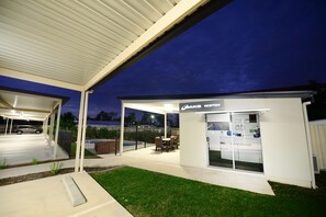A covered outdoor area with a reception desk, a car parked under a canopy, and a swimming pool in the background.