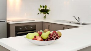 A kitchen with a white countertop, a bowl of fruit, and a vase with flowers. - Oaks Middlemount Suites (Middlemount)