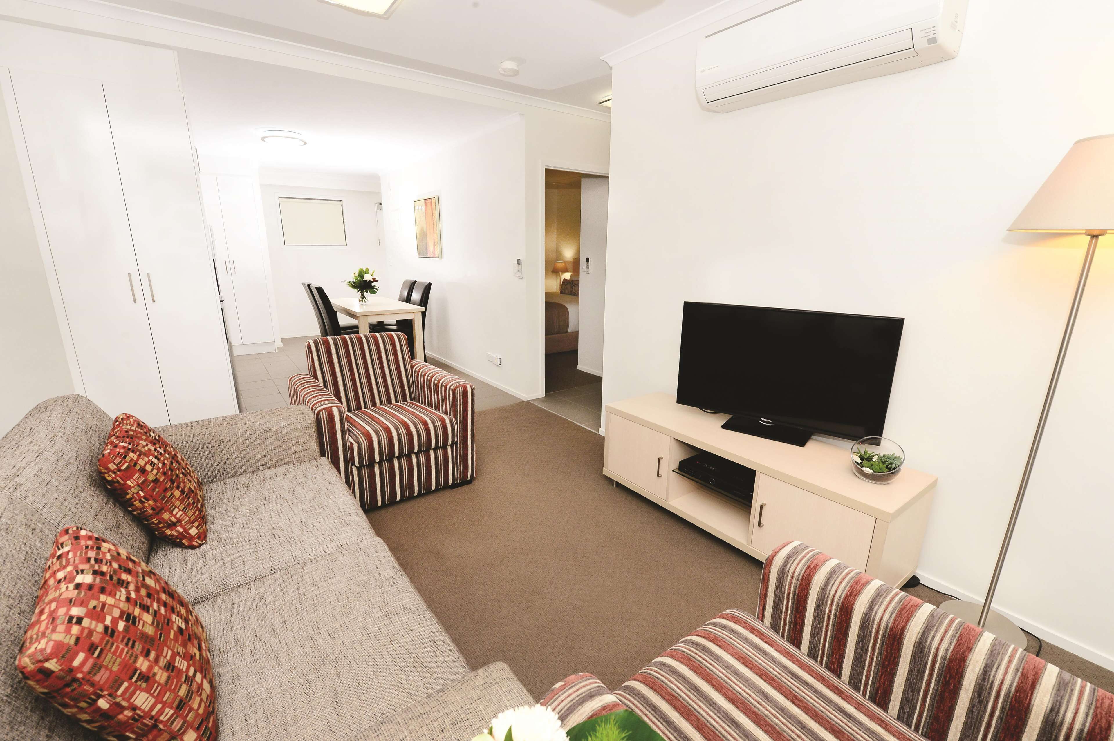 Una sala de estar moderna con un sofá, sillones a rayas, un televisor sobre un mueble bajo y una zona de comedor al fondo.